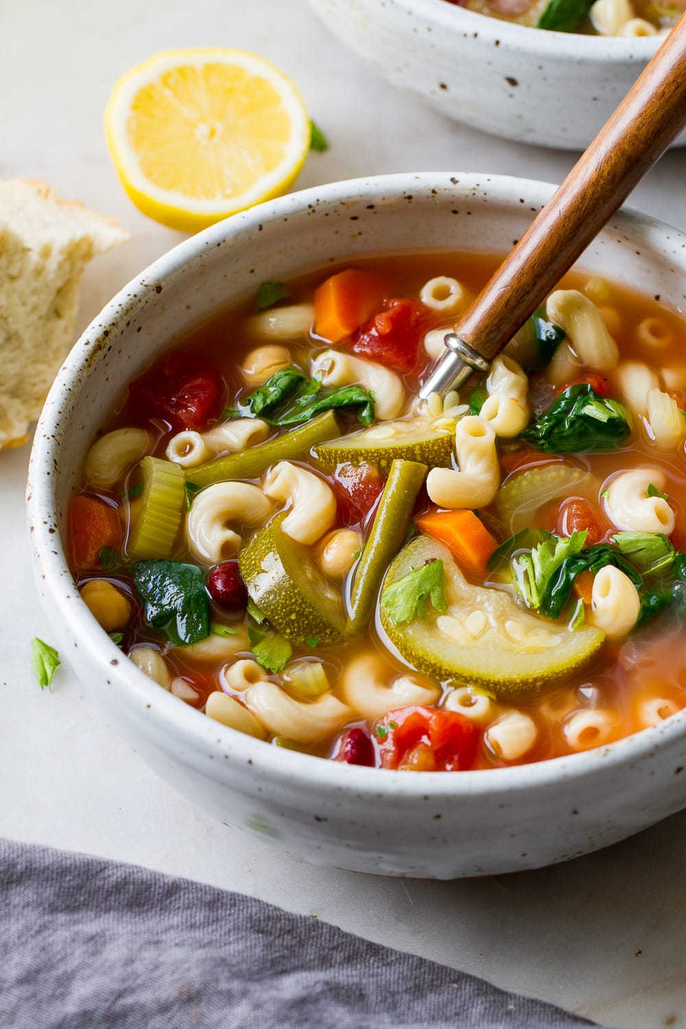 side angle view of healthy vegan minestrone soup in a bowl with wooden spoon.