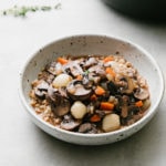 side angle view of handmade bowl with a serving of mushroom bourguignon and farro with items surrounding.