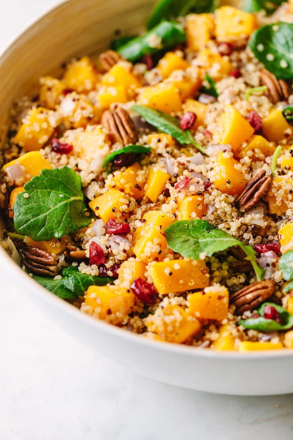 a side view of a large white serving bowl with autumn butternut squash and quinoa salad