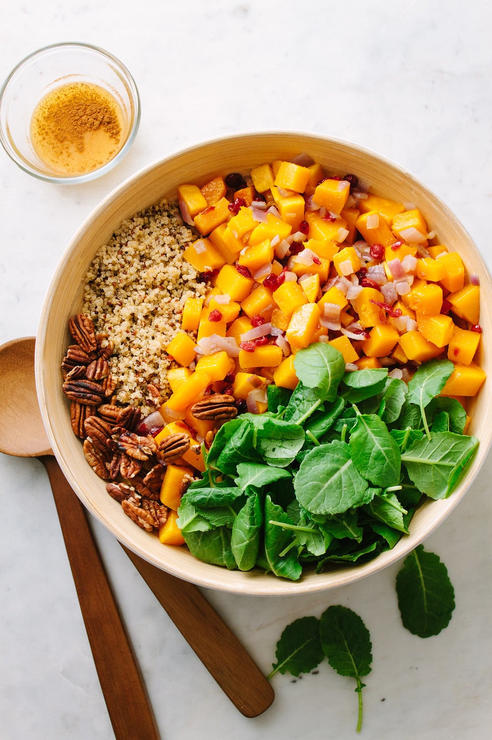 top down view of all the ingredients added to a bowl and ready to be mixed: ingredients include roasted butternut squash, quinoa, toasted pecans, baby spinach and cinnamon orange dressing