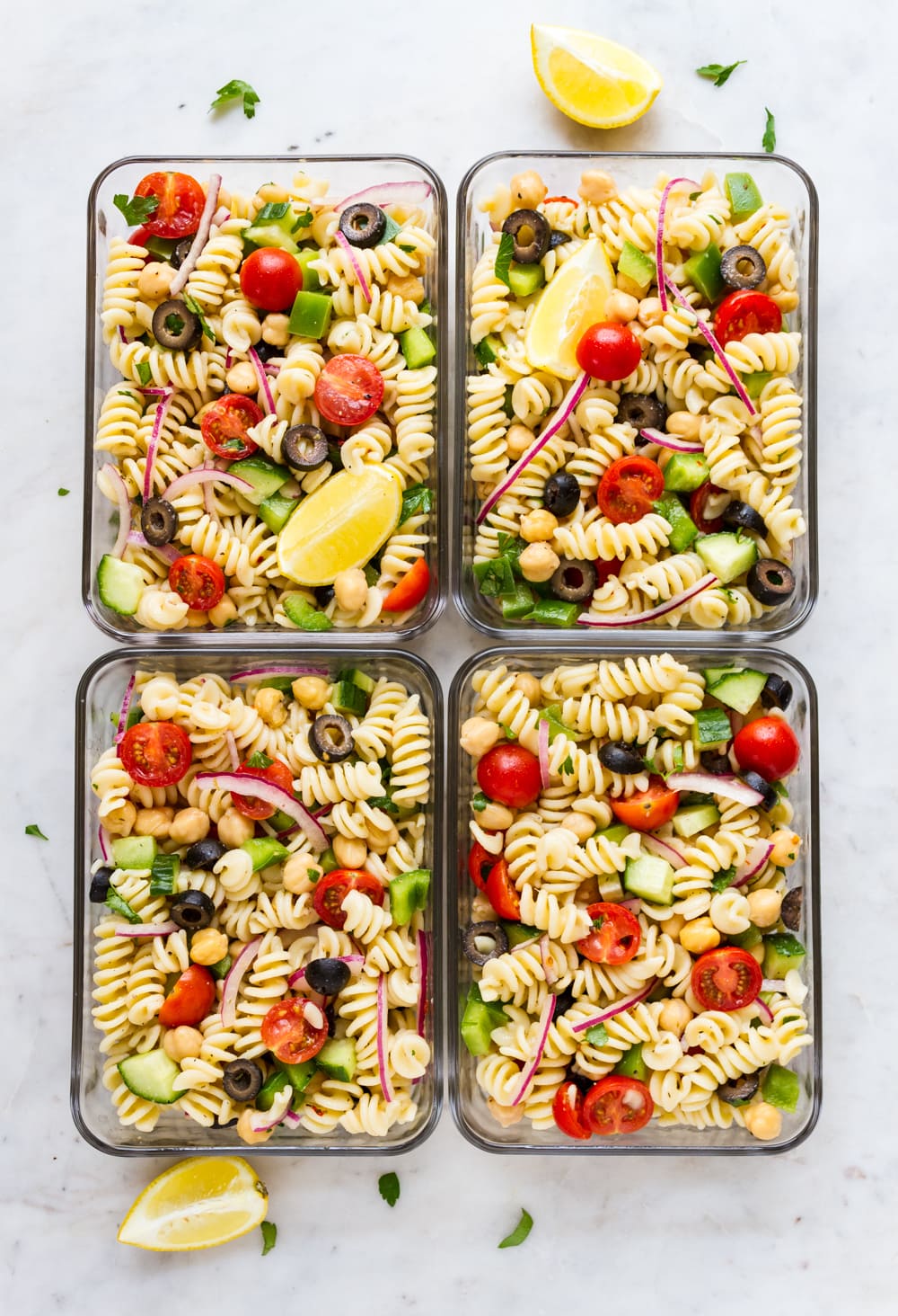 easy vegan pasta salad with lemon slice in individual storage containers for meal prep.