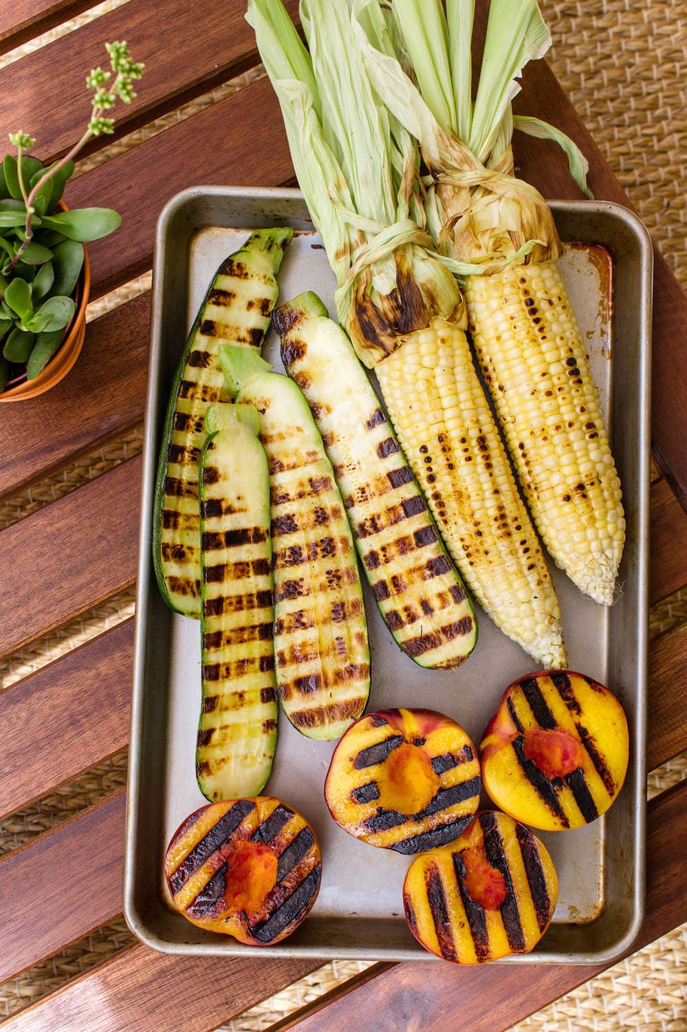 top down view of roasted zucchini, corn and peaches on a baking sheet.