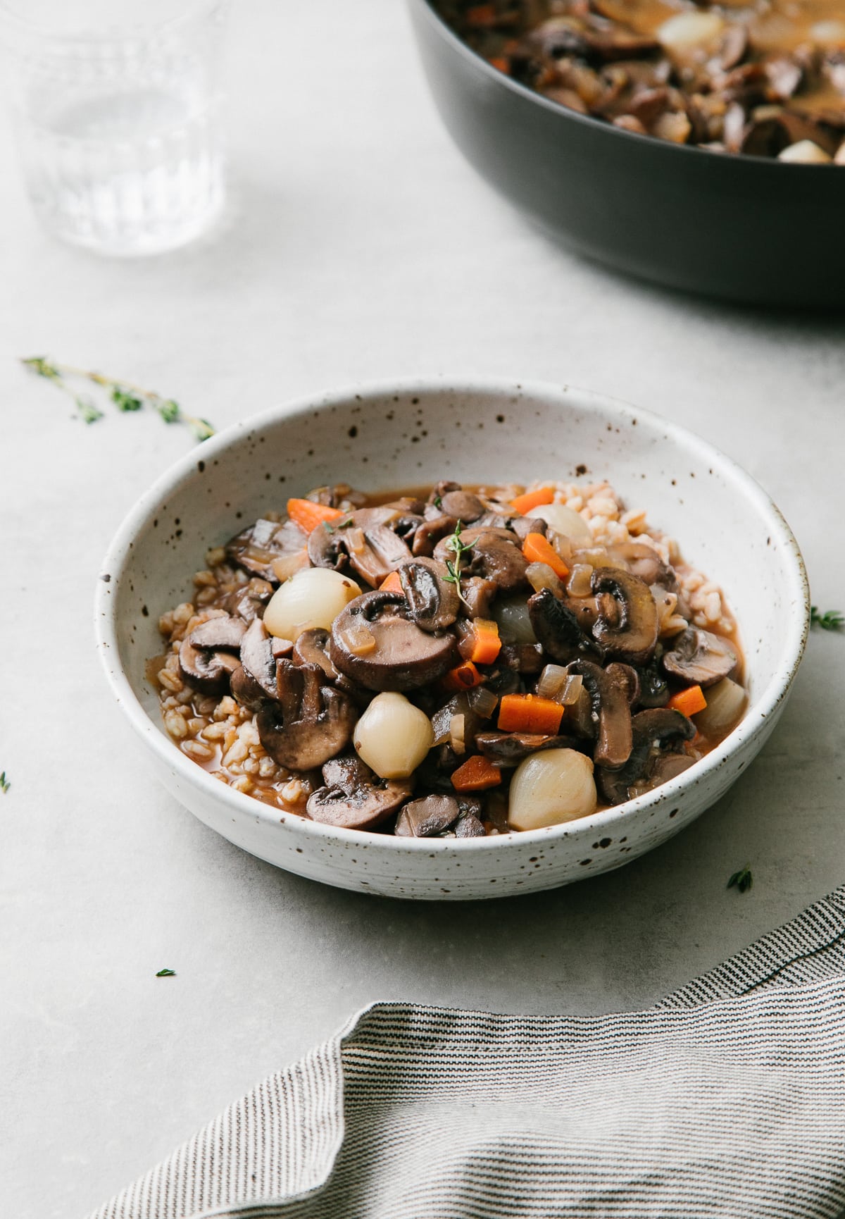 side anlge view of handmade bowl with a serving of mushroom bourguignon and farro with items surrounding.