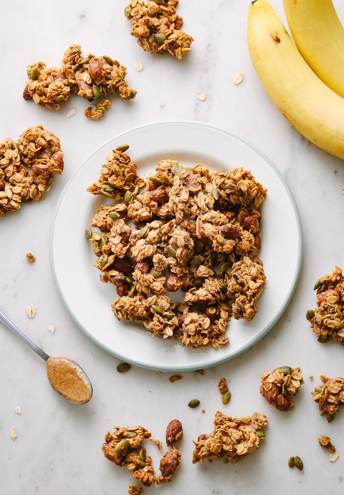 top down view of peanut butter banana granola clusters on a plate, surrounded by items.