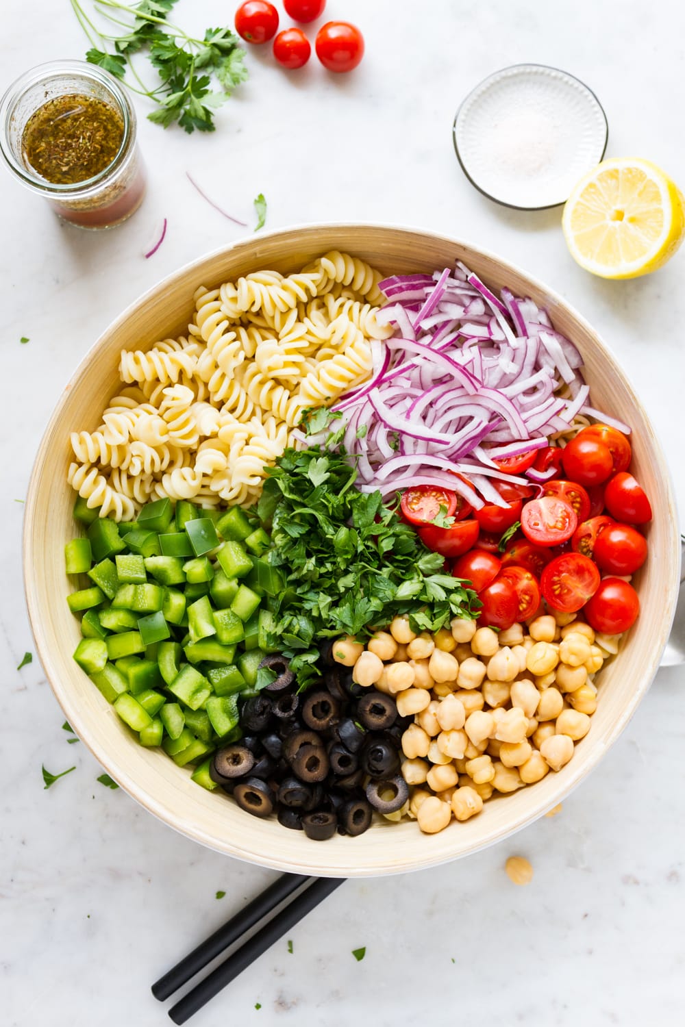 top down view of large mixing bowl with individual ingredients for vegan pasta salad added.